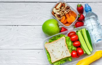 Lunchboxes filled with fresh vegetables and dried fruit and a bottle of water.