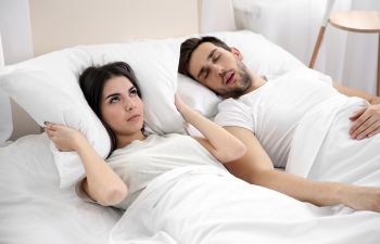 Annoyed young woman covering her ears with a pillow due to sleeping next to her man's snoring.