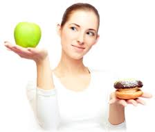 A slim woman with an apple in one hand and a donut in the other.
