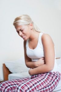 Woman in pyjamas with abdominal pain sitting on the edge of her bed.