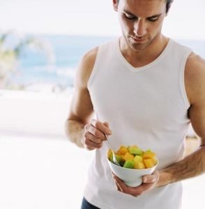 An athletic men eating fruit salad.