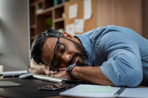 A fatigued man who has fallen asleep on his desk during work.